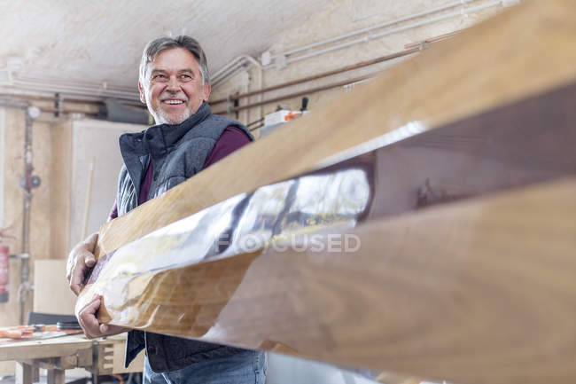 Tapete masculino sorridente carregando madeira acabada em oficina — Fotografia de Stock