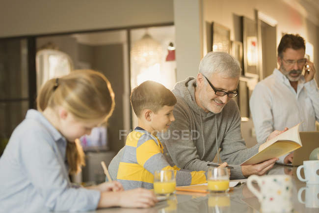 Male gay parents helping children with homework at counter — Stock Photo