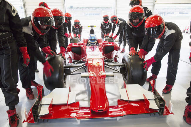 Pit tripulação empurrando fórmula um carro de corrida na garagem de reparação — Fotografia de Stock