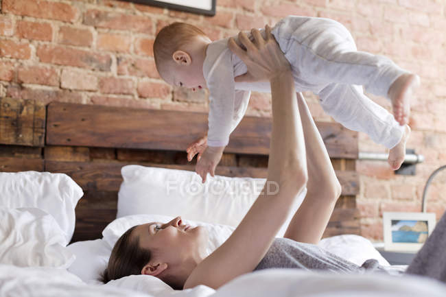 Mother lifting baby daughter overhead on bed — Stock Photo