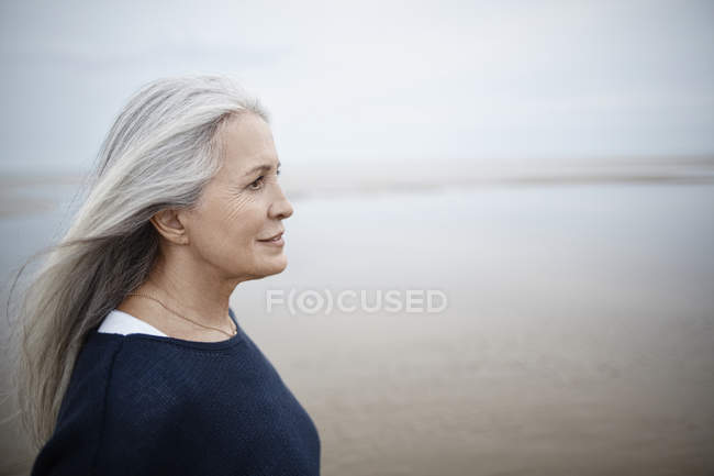 Pensiva donna anziana guardando lontano sulla spiaggia invernale — Foto stock