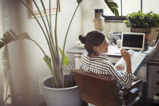 Empresária lendo papelada com os pés na mesa — Fotografia de Stock