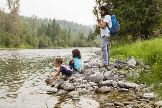 Father and daughters hiking, resting at lakeside — Stock Photo
