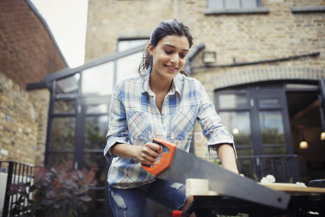 Junge Frau mit Säge beim Holzschneiden auf Terrasse — Stockfoto