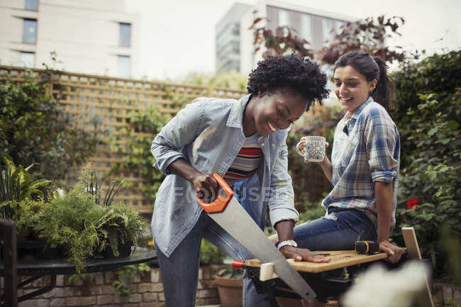 Women drinking coffee and cutting wood with saw on patio — Stock Photo