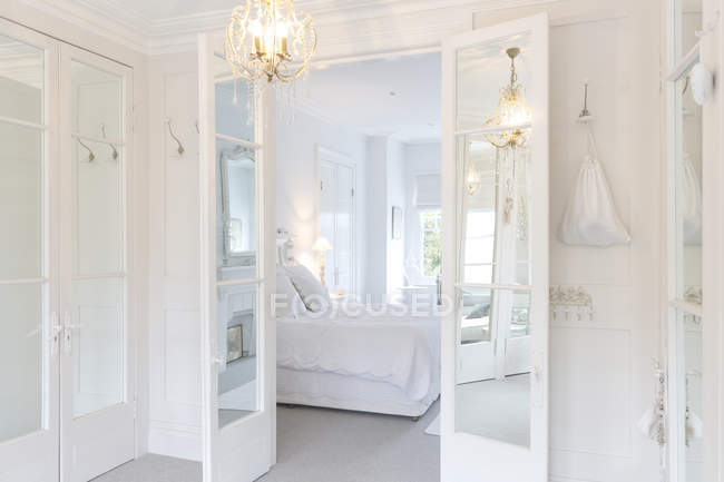 Blanco, casa de lujo escaparate dormitorio interior con puertas francesas y lámpara de araña - foto de stock