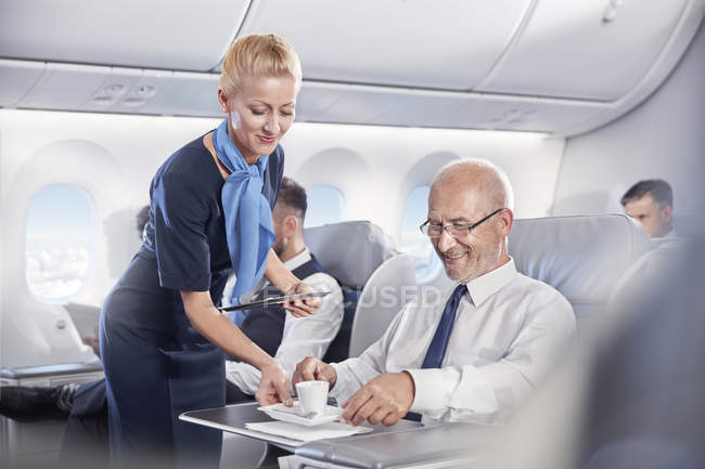 Flight attendant serving espresso coffee to businessman in first class on airplane — Stock Photo