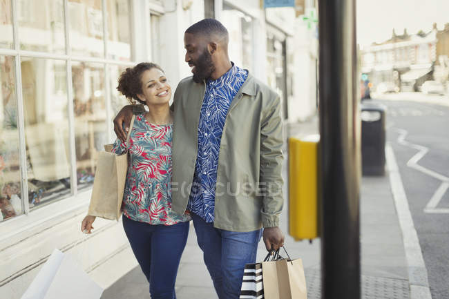 Liebenswertes junges Paar mit Einkaufstüten spaziert an urbanen Schaufenstern entlang — Stockfoto