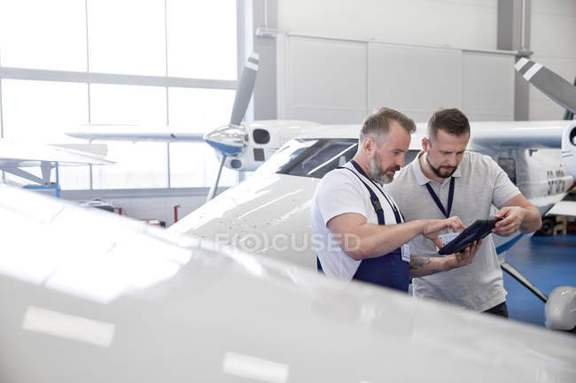 Инженеры-механики используют цифровой планшет возле самолета в ангаре — стоковое фото