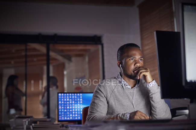 Serious, focused businessman with headphones working late at computer in dark office at night — Stock Photo