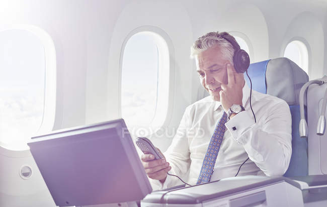 Empresário com fones de ouvido assistindo filme no avião — Fotografia de Stock