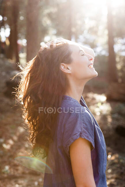 Посміхаючись, безтурботна жінка в сонячному лісі — стокове фото