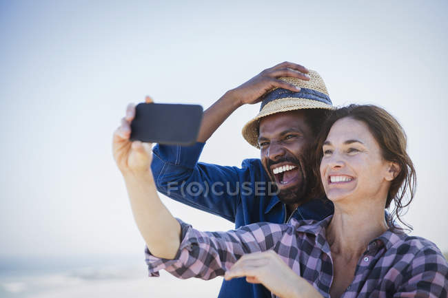 Смеющаяся, энергичная многонациональная пара делает селфи с камерой телефона — стоковое фото