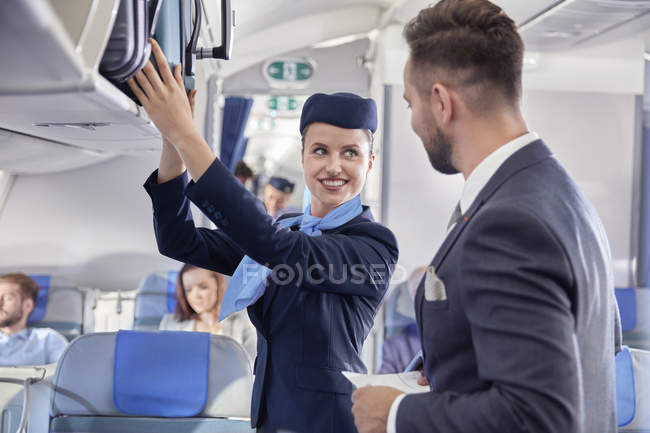 Asistente de vuelo ayudando a hombre de negocios con el equipaje en el avión - foto de stock