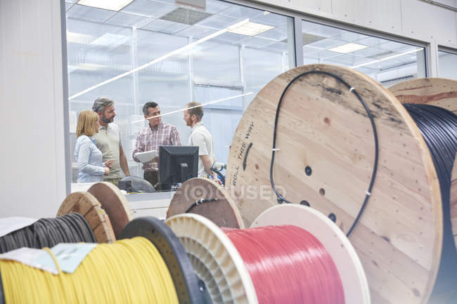 Supervisores conversando no escritório atrás de carretéis na fábrica de fibra óptica — Fotografia de Stock