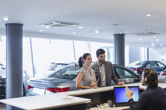 Couple customers talking to male receptionist at desk in car dealership showroom — Stock Photo