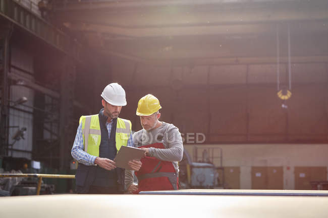 Hombre capataz y trabajador con portapapeles hablando en fábrica - foto de stock