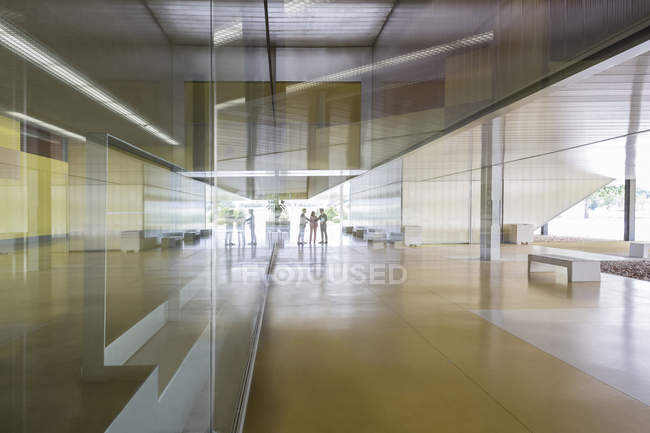 Gente de negocios apretón de manos en la distancia en el pasillo moderno vestíbulo de la oficina - foto de stock