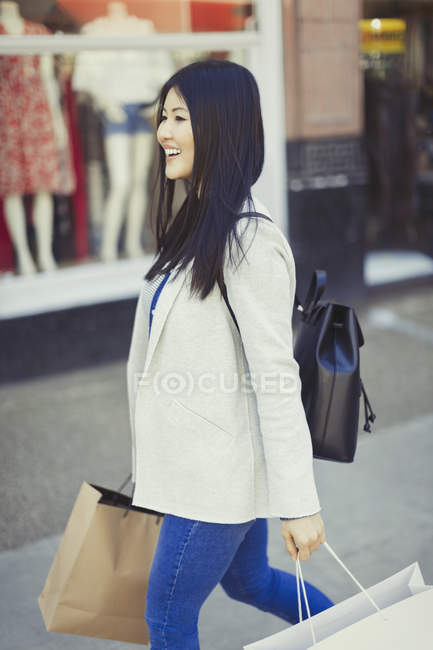Улыбающаяся молодая женщина, идущая вдоль витрины с сумками — стоковое фото