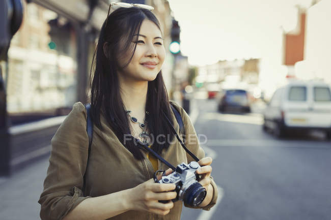 Усміхнена молода жінка-туристка фотографується з камерою на міській вулиці — стокове фото