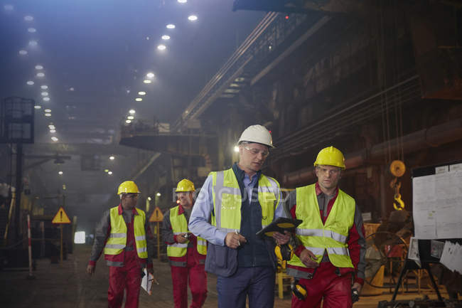 Superviseur et métallurgistes marchant et parlant dans une aciérie — Photo de stock