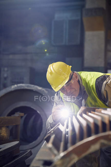 Focused steelworker with flashlight examining steel part in steel mill — Stock Photo