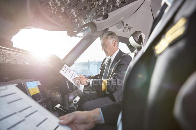 Male pilots with clipboard preparing in airplane cockpit — Stock Photo