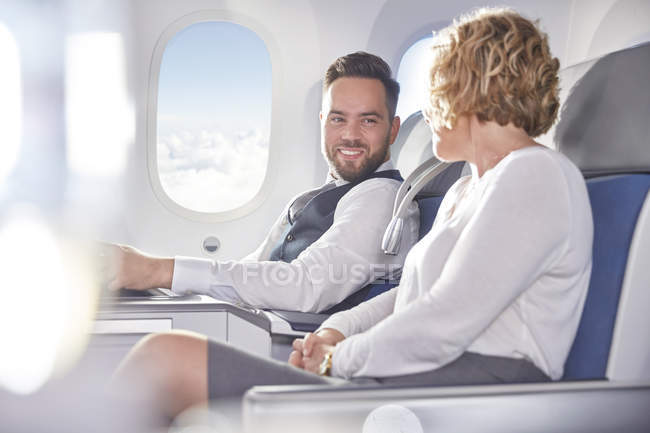 Smiling businessman and businesswoman talking on airplane — Stock Photo