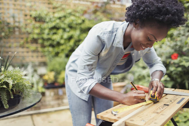 Woman with tape measure measuring wood on patio — Stock Photo