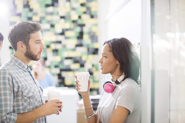 Gente creativa de negocios con café y auriculares hablando en la oficina - foto de stock