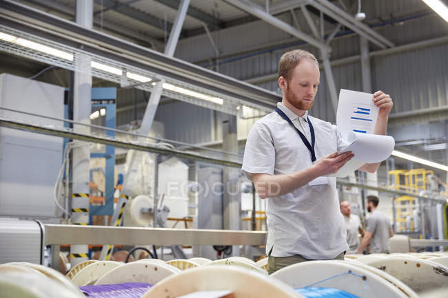 Superviseur masculin avec contrôle de l'inventaire du presse-papiers dans l'usine de fibre optique — Photo de stock