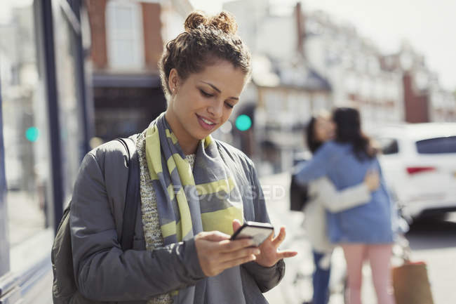 Молода жінка смс на сонячній міській вулиці — стокове фото