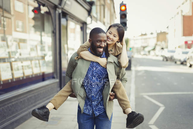 Playful young couple piggybacking on urban street — Stock Photo