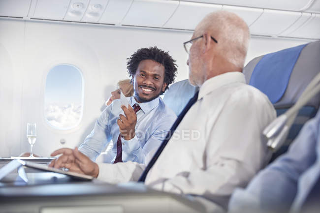 Des hommes d'affaires souriants échangeant des cartes de visite en avion — Photo de stock