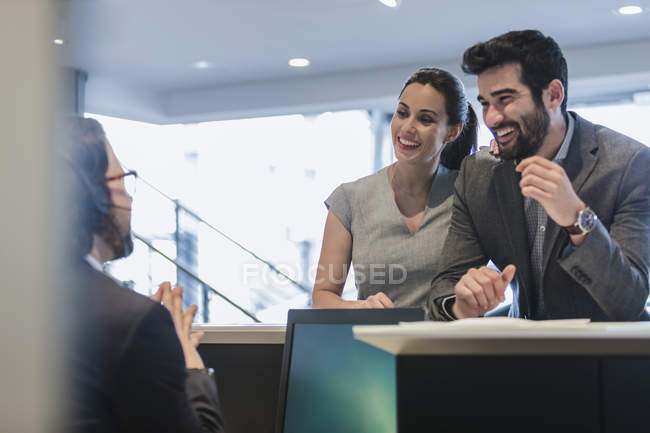 Smiling couple customers talking to receptionist at desk in car dealership — Stock Photo