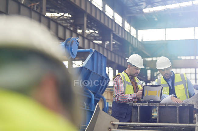 Male foreman and engineer working at laptop, discussing blueprints in factory — Stock Photo