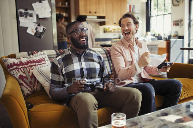 Des hommes riants amis jouant au jeu vidéo sur le canapé du salon — Photo de stock