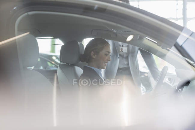 Smiling cliente do sexo feminino sentado no assento do motorista de carro novo na concessionária de automóveis — Fotografia de Stock