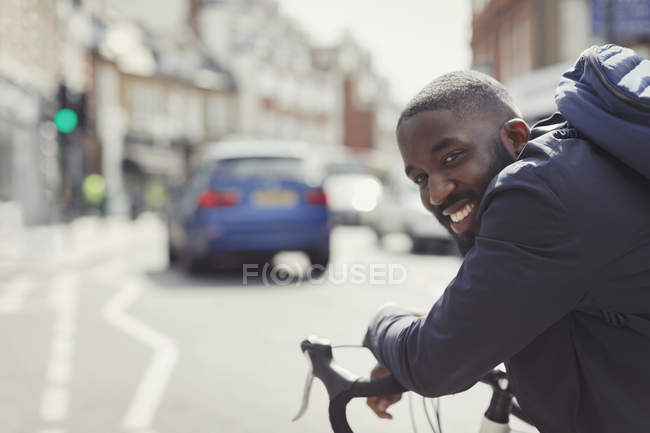 Un jeune homme d'affaires souriant qui se déplace à vélo sur une rue urbaine ensoleillée — Photo de stock