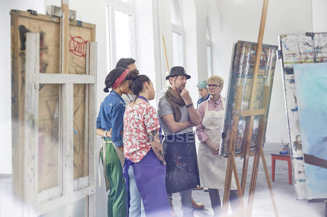 Art students and instructor examining, critiquing painting in art class studio — Stock Photo