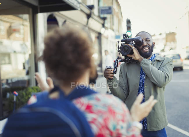 Jeune homme avec caméra vidéo vidéo femme dans la rue — Photo de stock