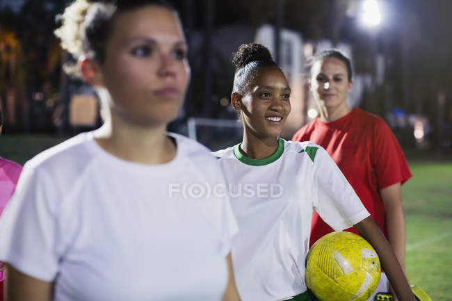 Sonrientes, confiadas jóvenes futbolistas en el campo por la noche - foto de stock