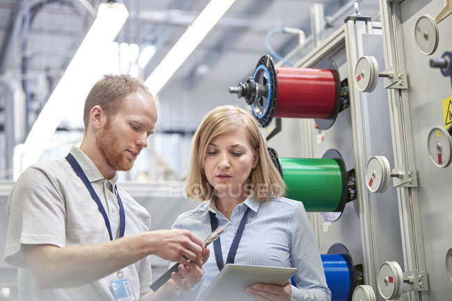 Travailleurs masculins et féminins avec tablette numérique examinant la partie dans l'usine de fibre optique — Photo de stock