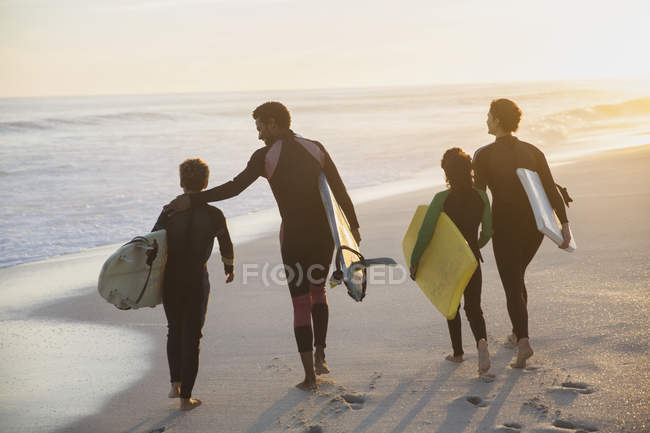 Surfistas familiares caminando con tablas de surf en la soleada playa del atardecer de verano - foto de stock