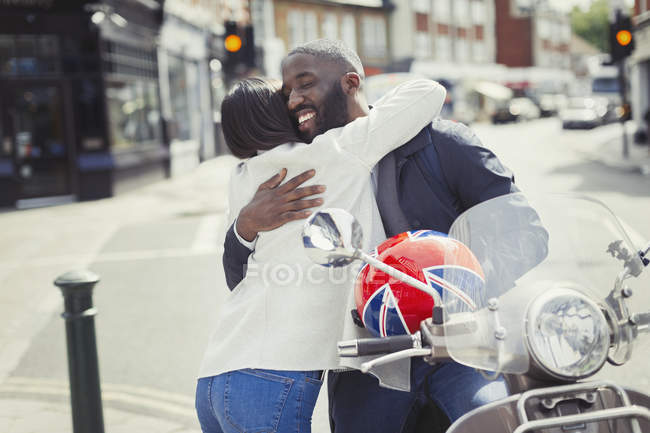 Прихильна молода пара обіймається моторолером на сонячній міській вулиці — стокове фото