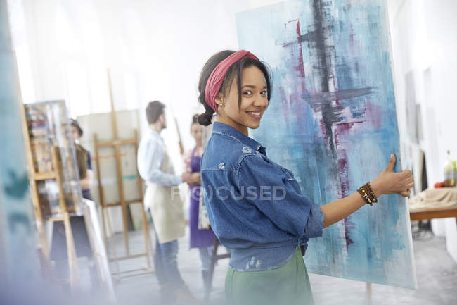Portrait smiling female artist lifting painting in art class studio — Stock Photo
