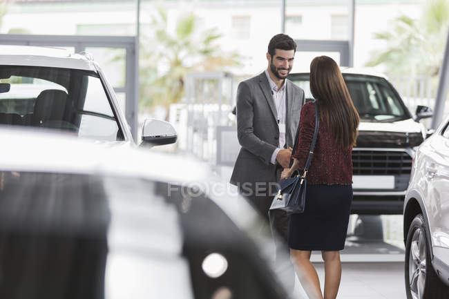 Car salesman greeting, shaking hands with female customer in car dealership showroom — Stock Photo