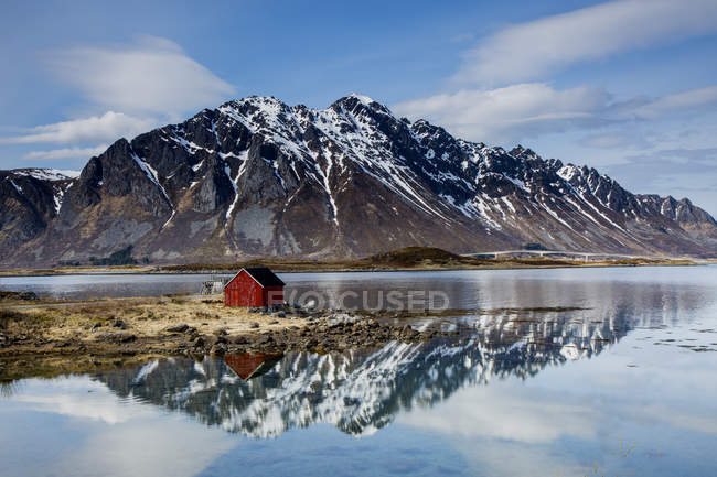 Cabaña de pesca remota en el fiordo frente al mar debajo de las montañas escarpadas, Kleppstad, Austvagoya, Noruega - foto de stock