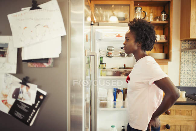 Hungry woman peering into refrigerator in kitchen — Stock Photo