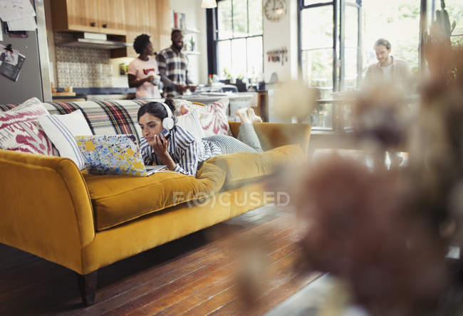 Young woman with headphones using laptop on living room sofa — Stock Photo